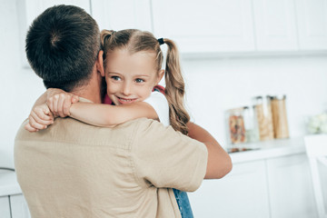 Fototapeta premium father and smiling daughter with backpack hugging each other in kitchen at home, back to school concept