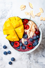 Acai breakfast superfoods smoothie bowl with mango, blueberry, cherry, coconut flakes. Overhead, top view, flat lay.