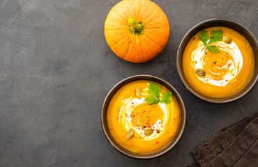 Pumpkin soup in a bowl with fresh pumpkins, garlic and parsley herbs on a black background. Autumn...