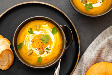Pumpkin soup in a bowl with fresh pumpkins, garlic and parsley herbs on a black background. Autumn concept.