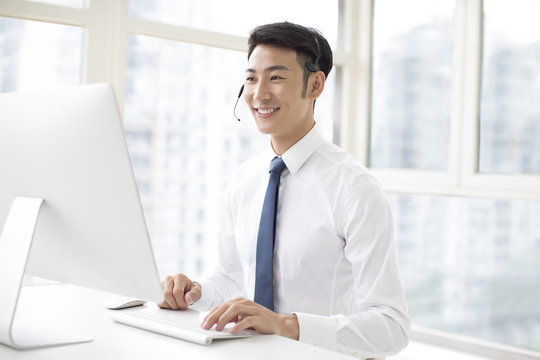 Cheerful young businessman working in office with headset