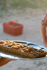 Unrecognizable person serving a pear and almond tart outdoor. Selective focus, illuminated by warm sunset light.
