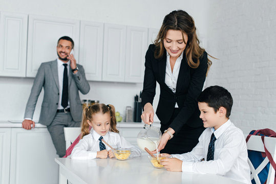 smiling mother pouring milk into sons bowl during breakfast in kitchen at home