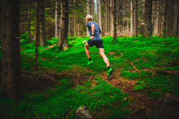Obraz premium Athletic man running on trail through green forest. Sport photo, trail