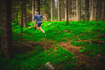 Male runner running on a green forest trail.