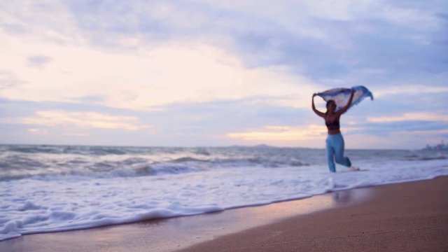 Silhouette attractive young asian woman with sunglasses running on beach holding waving scarf on beautiful windy with twilight in sunset,Slow motion footage