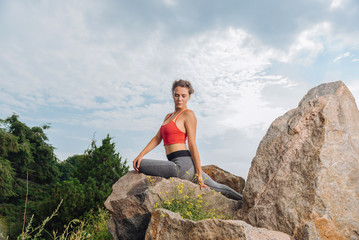 Naklejka na ściany i meble Resting after workout. Curly slim woman feeling relaxed and calm sitting on rock while resting after workout