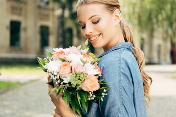 Fototapeta premium smiling young woman looking at flower bouquet