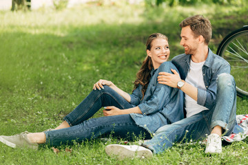 Naklejka na ściany i meble happy young couple sitting on grass at park together