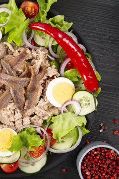 Salad with tuna, anchovies and vegetables. Mediterranean food. The background is black. Top view. Copy space. Vertical shot.