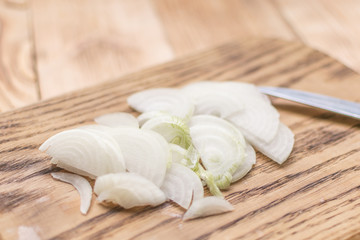Sliced onions with half rings on a wooden chopping board on a wooden background.