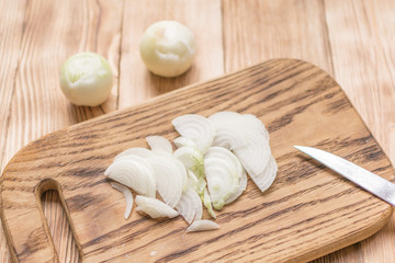 Sliced onions with half rings on a wooden chopping board on a wooden background.