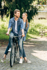 beautiful young couple riding vintage bicycle together at park