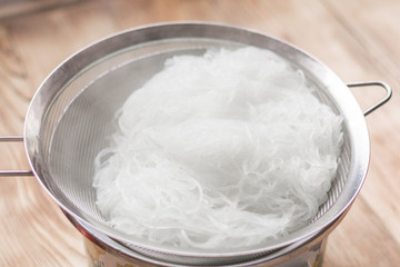 Boiled hot steaming rice noodles, spaghetti in a colander.