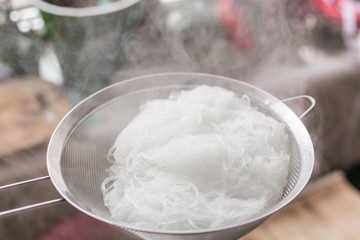 Boiled hot steaming rice noodles, spaghetti in a colander.