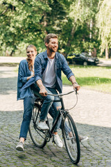 happy young couple riding bicycle together at park