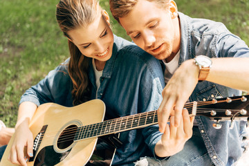 close-up shot of young happy woman learning to play guitar with boyfriend at park