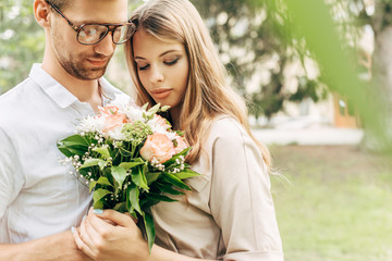 close-up shot of stylish young couple with bouquet embracing outdoors