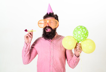 Man with beard and mustache on happy face holds air balloons, white background. Party concept. Guy in party hat with party horn celebrates. Hipster in giant sunglasses celebrating birthday