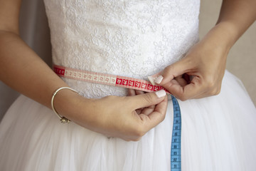 Bride measuring her waist in wedding dress