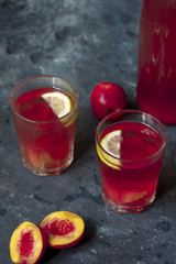 Two glasses of peach-raspberry lemonade with lemons and peaches on rustic background
