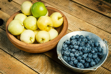 delicious and fresh blueberries and apples in bowls on a wooden table