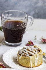 Cinnamon roll with white glazed icing on the top with the cup of coffee