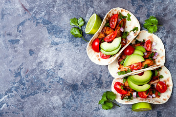 Mexican grilled chicken tacos with avocado, tomato, onion on rustic stone table. Recipe for Cinco...
