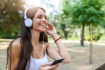 Beautiful girl listening music using smartphone in public park