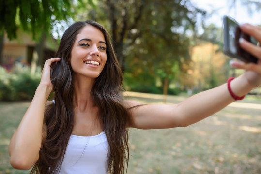 Young Beauty with long brown hair looking at smartphone taking photo of herself