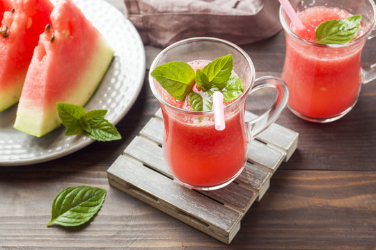 Watermelon sliced on a plate with mint leaves and fresh watermelon smoothie on a wooden background.