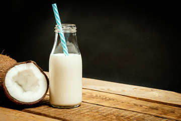 fresh brown coconuts and bottle of milk on a wooden table on a black background