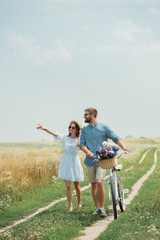 smiling couple in sunglasses with retro bicycle in summer field with wild flowers