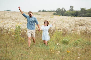 Naklejka na ściany i meble happy lovers holding hands while running in meadow with wild flowers