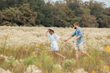 Naklejka na ściany i meble side view of young lovers holding hands while walking together in field with wild flowers