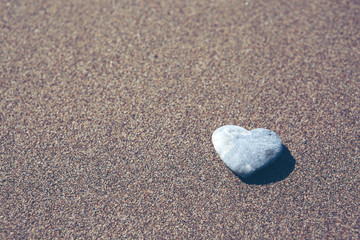 Fototapeta na wymiar Gray stone in the form of heart lies on sand.