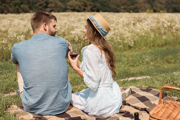 back view smiling couple having picnic on summer meadow with wild flowers around