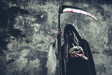 Demon witch holding pumpkin in hand with bloody reaper on grunge wall background. Halloween and...