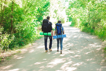 Obraz premium Young couple hikers in forest. sports man and woman with backpacks on road in nature