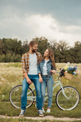 smiling lovers with retro bicycle looking at each other in field with wild flowers