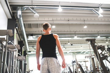 Young man in modern crossfit gym, standing. Rear view.