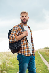 portrait of handsome pensive man with black leather backpack looking away in field