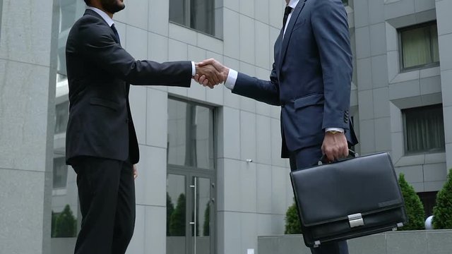 Two company workers in formal suits shaking hands, colleagues greeting, merger