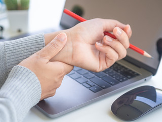 Closeup woman holding her wrist pain from using computer long time. Office syndrome concept.
