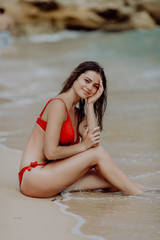 Attractive young woman wearing a red bikini sits on a seabeach