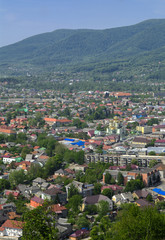 Fototapeta premium Colorful exalted view from a bird's eye view to houses in residential district in the city of Khust, Western Ukraine with high mountains in the background on a background of green vegetation.