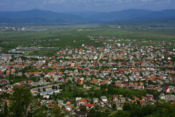 Fototapeta na wymiar Colorful exalted view from a bird's eye view to houses in residential district in the city of Khust, Western Ukraine with high mountains in the background on a background of green vegetation.
