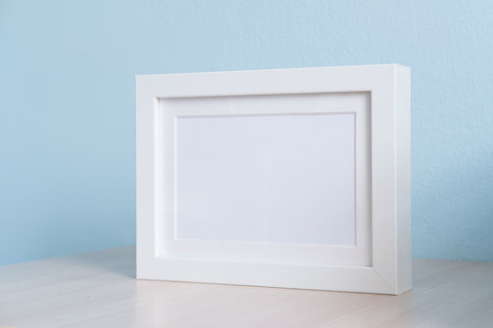 blank white picture frame on the table wood with blue background