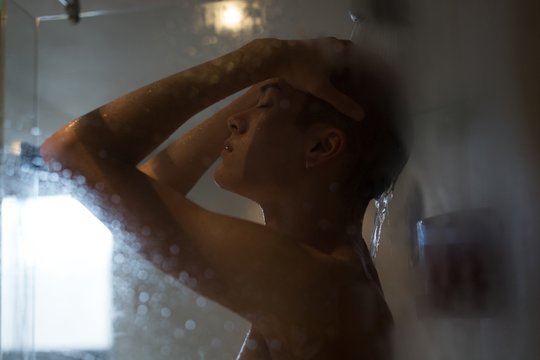 Androgynous young man taking shower in bathroom