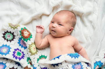 Newborn baby lying on bed, covered by a crocheted blanket. Top view.